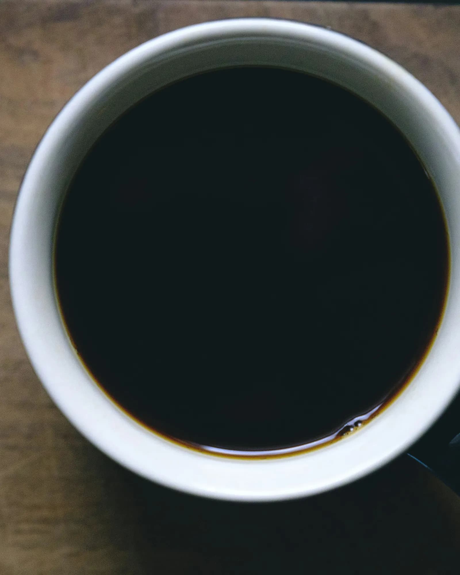 A white mug of black coffee seen from above on a weathered wooden table